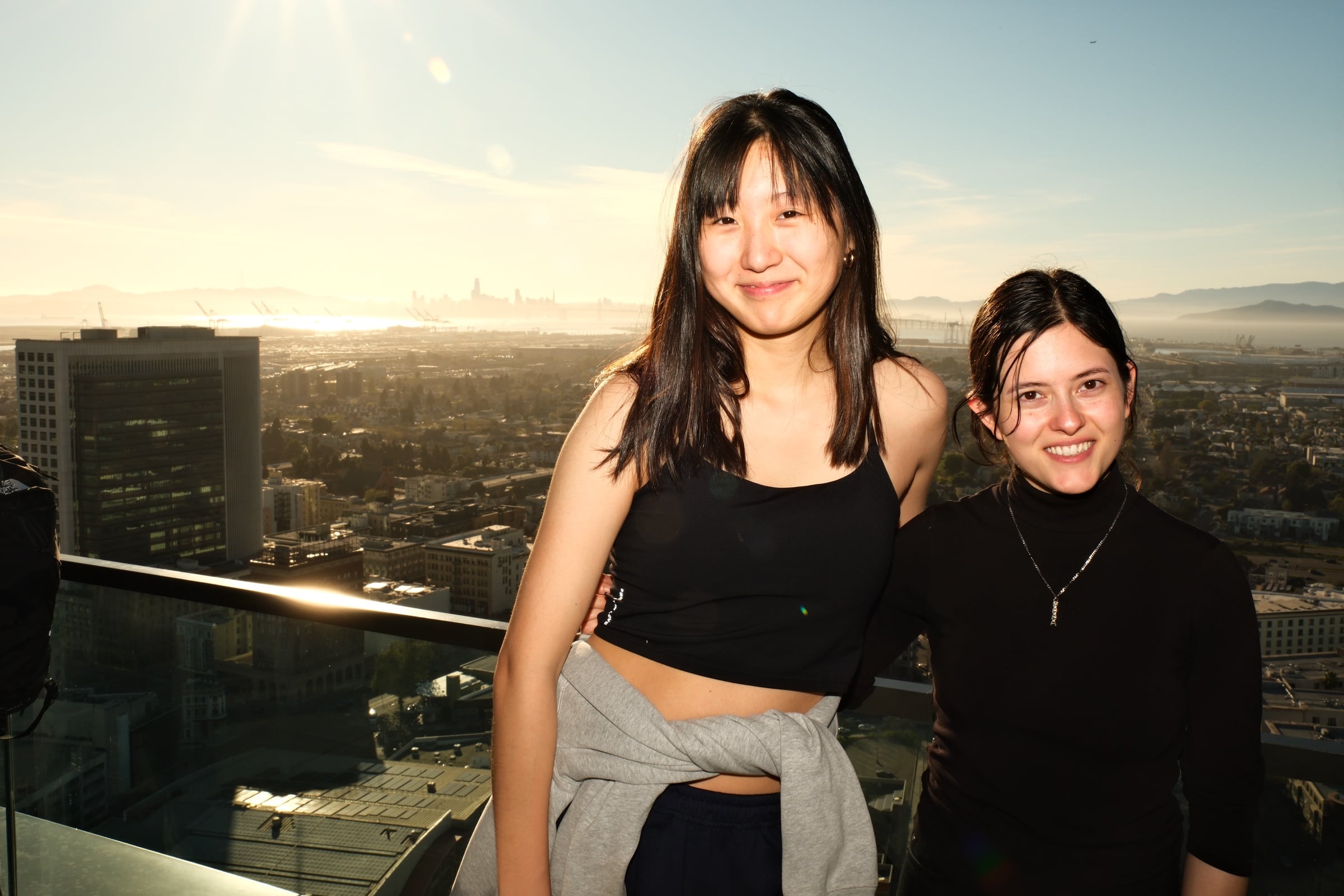 Two attendees on the rooftop terrace with the Bay and SF skyline at golden hour