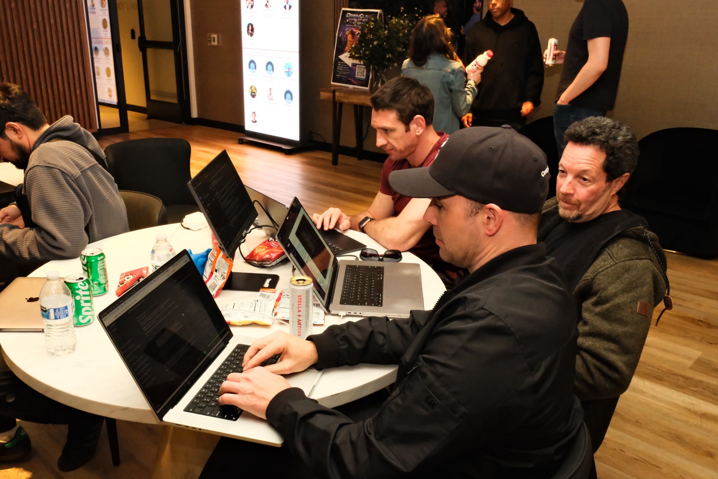 Participants hacking at a table with laptops and Stella Artois, OpenClaw poster in background
