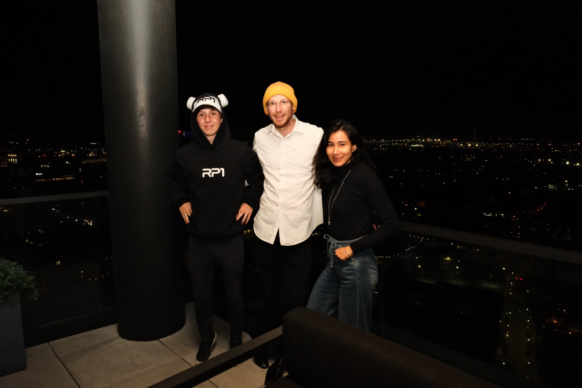 Three attendees on the rooftop terrace at night with city lights behind them