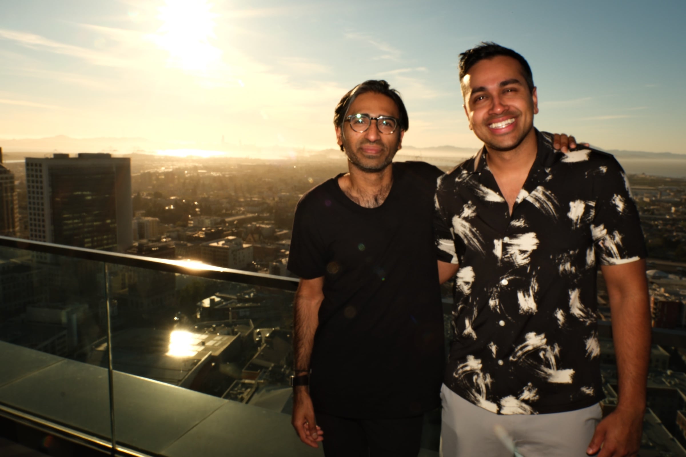 Two attendees on the rooftop at sunset with Oakland skyline